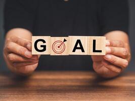 Hands holding wooden cubes with letters GOAL and dartboard icon while sitting at the table photo