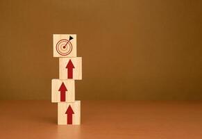 Wooden blocks stacked with red arrows point to the dartboard icon on a brown background photo