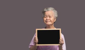 An elderly Asian woman holding a mini blackboard and looking at the camera with a smile while standing on a gray background photo