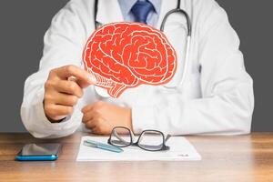Doctor in a uniform holding a brain symbol made from red paper while sitting at the table photo