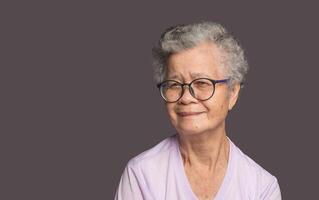 Senior Asian woman looking at the camera with a smile while standing on a gray background photo