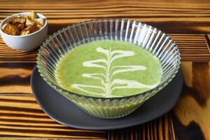 Broccoli Soup on wooden table with crackers side view photo