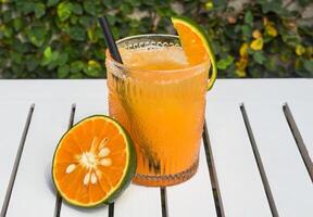 Orange juice with ice on white wooden table with slice of orange and copy space photo