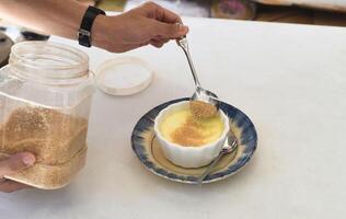 Process of sprinkling brown sugar on the Creme brulee on white background photo