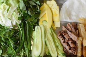 Fresh greens with sliced unripe mango and roasted meat on table ready for cooking spring rolls photo