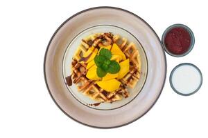 Belgium waffles with sliced mango on plate with tropical topping and yogurt sauce photo