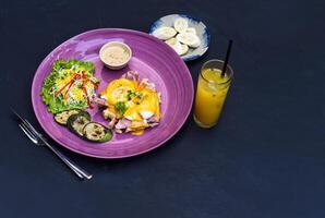 Eggs Benedict poached eggs on grilled ham with holland sauce on belgian waffle with grilled zucchini with plate of banana and cup of passion juice photo