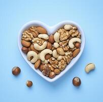 heart shaped bowl filled with mixed nuts including cashews, almonds, and walnuts, perfect for healthy snack or decoration photo