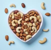 heart shaped bowl filled with mixed nuts, including cashews, almonds, and walnuts, on light blue background creates delightful and healthy snack photo
