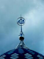 Blue and white mosque dome with an Arabic Calligraphy written Allah on top is on top of a building. The dome is located on a cloudy day. Islamic Ramadan Background. photo