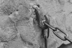 Rusty chain hook attached to a weathered stone wall in an old structure showcasing historical craftsmanship in grayscale photo