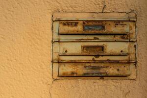 Weathered mailboxes attached to a textured wall in a quiet urban setting during late afternoon light photo