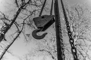 Vintage pulley hanging from a chain against a backdrop of bare trees in winter sunlight photo