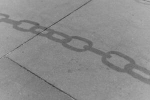 Shadows of a chain on concrete surface revealing a connection to the past in an urban environment photo