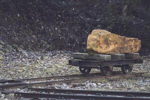 Heavy stone block on a wooden cart along old railway tracks in a forest clearing during daylight photo