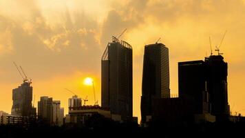 Dynamic progress of a city skyline as towering cranes work on a complex of skyscrapers against a breathtaking sunset. video