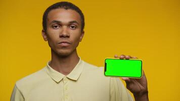 Man Displaying Smartphone with Green Screen on Yellow Background video