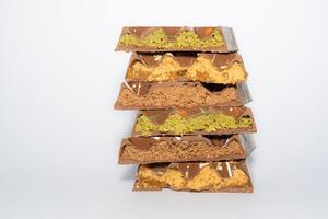 Stack of Trend Dubai chocolate with pistachio paste, peanut butter, caramel, chocolate spread and kunafa dough. With copy space. confectionery. photo