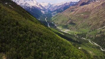 Stunning alpine valley with greenery, forested slopes, river, snow-capped peaks video
