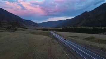 Aerial view of a valley with a river and road surrounded by mountains at sunset video
