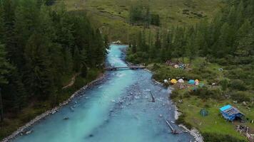 Aerial view of the turquoise river flowing in the forest near the tents on the bank video