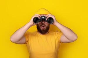 surprised man looking into binoculars on yellow photo