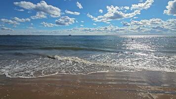 Sunny seashore with gentle waves, blue sky and white clouds reflecting on the water surface. video