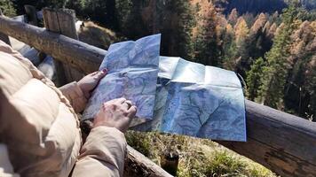 A person in a beige jacket examines a map against a scenic forest backdrop adventure, exploration video