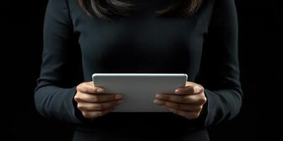 Person holding a tablet while wearing a black outfit against a dark background in a modern setting photo