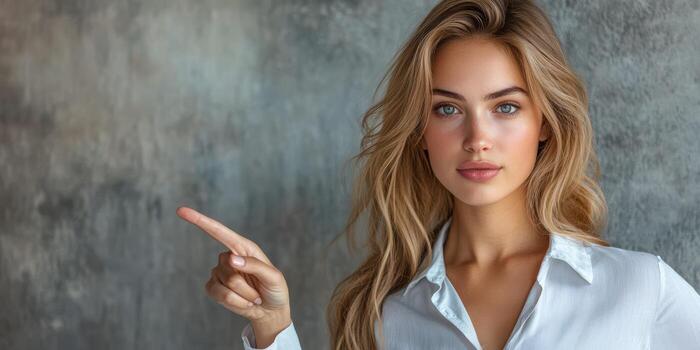 Woman with long hair points thoughtfully against a textured gray background in a casual setting photo