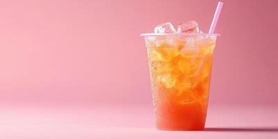 Refreshing iced drink with ice cubes and straw against a pink background during a warm sunny day photo