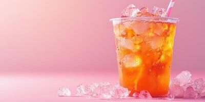 Refreshing iced tea in a plastic cup with ice cubes and a straw against a pink background during summer photo