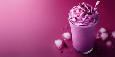 Purple smoothie topped with whipped cream and garnished with candy, served in a clear glass against a vibrant pink background photo