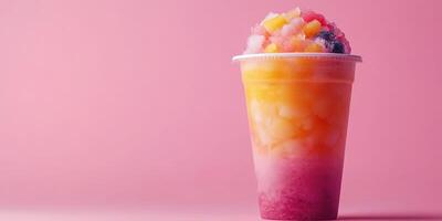 Colorful shaved ice dessert with assorted fruits and vibrant layers served in a clear cup against a pink background photo