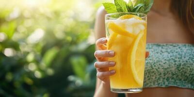 Refreshing summer beverage with citrus slices and mint held outdoors in a lush green setting photo