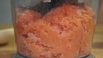 Large pieces of fresh chicken meat are chopped into small pieces and turned into minced meat using a glass electric blender in the home kitchen. close-up video