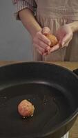 Chef, wearing an antique apron, prepares meatballs according to classic Scandinavian recipe. She gathers ground meat, shapes it into ball, and then cooks it in pan. vertical video