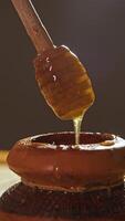 Viscous and mouth-watering honey molasses or maple syrup are extracted using a special spoon from an old brown pot. Vertical. video