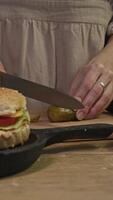 Pickled cucumbers are cut into thin, round pieces and then added to a classic American hamburger with a cutlet and other vegetables. video