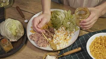 Chef prepares delicious salad with corn, tuna, and special sauce. She makes sauce by adding Dijon mustard to sour cream and mayonnaise, then mixing everything thoroughly. video