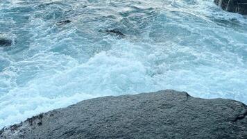 The waves of a chilly, clear blue sea or ocean, with splashes, beat against a large boulder and roll back. video