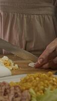 cuisinier coupes cuit dur poulet Oeuf dans petit pièces sur en bois conseil, portant un tablier, à ajouter il à salade avec maïs. verticale video