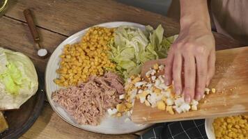 Chef prepares delightful salad with variety of ingredients, which are not mixed together on plate. salad includes corn, tuna, iceberg lettuce, and boiled egg. video