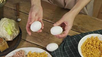 Chef prepares salad following French recipe, using eggs, corn, tuna, and lettuce. She peels eggs' shells and adds them to salad. video