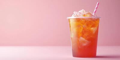 Iced tea served in a clear cup with a straw on a light pink background photo