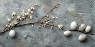 Decorative branch with flowers and assorted eggs laid on a textured gray surface for a spring celebration photo