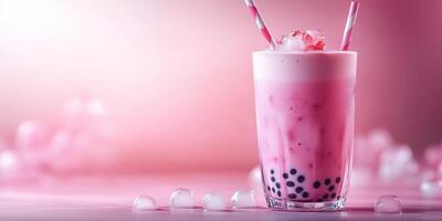 Refreshing pink drink with tapioca pearls served in a clear glass with striped straws and ice cubes against a soft pink background photo