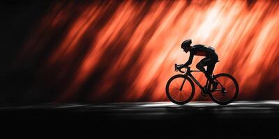 Cyclist racing along a lit pathway at sunset creating a dynamic silhouette under warm orange and dark hues photo