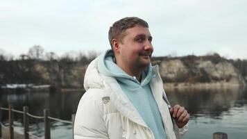 Close-up portrait of smiling young handsome man standing alone outdoors at river bank in mountains and looking at camera. Young male looking at camera and smiling. video