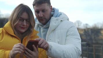 Portrait of a happy young Caucasian couple having fun together at the lake park, looking at mobile phone video